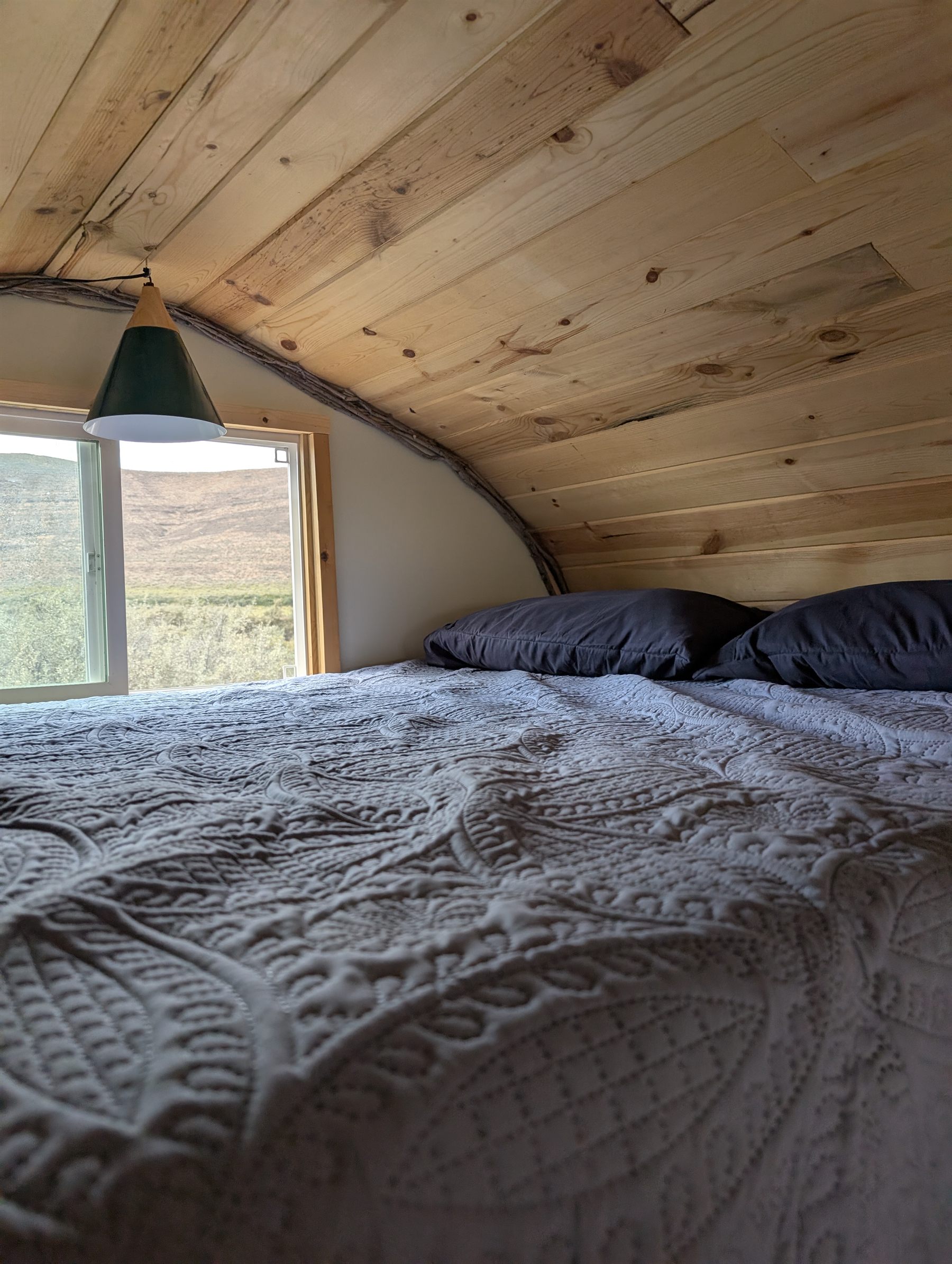 A made bed under the cabin's curved knotty-pine ceiling